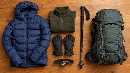 Winter trekking gear laid out on a wooden floor including down jacket, fleece, gloves, trek pole and backpack
