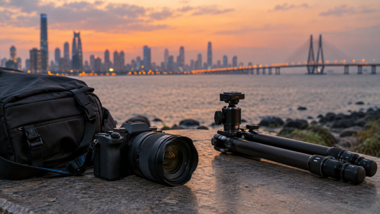 Mirrorless camera with lens beside a tripod and camera bag with the Mumbai skyline and sea link at dusk