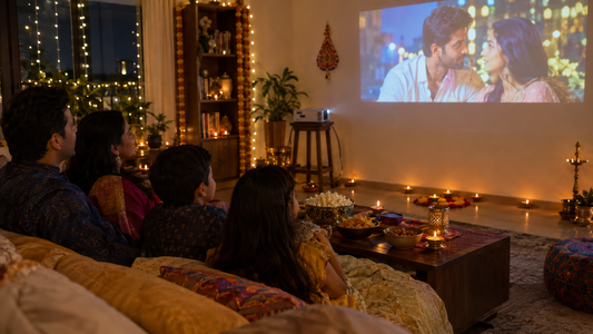 Family watching a film projected on a living room wall decorated with Diwali lights and diyas