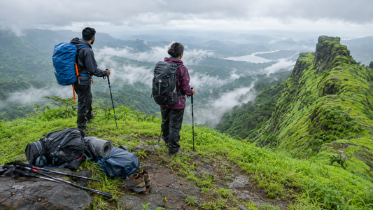 Two trekkers with rented backpacks and poles on a green Sahyadri ridge in monsoon